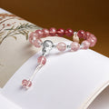 Gradient strawberry crystal bracelet with blessing plaque and gourd resting on a book