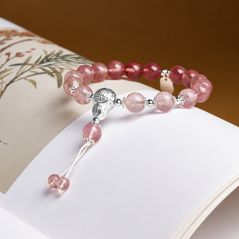 Gradient strawberry crystal bracelet with blessing plaque and gourd resting on a book