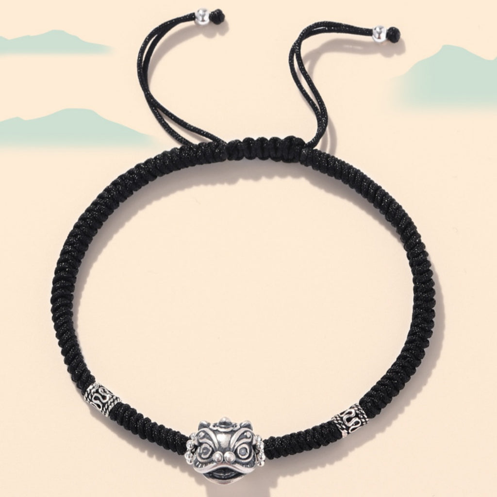 Black braided cord bracelet with an oxidized silver guardian lion face and engraved spacer beads.
