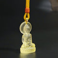 Amber Liuli Shakyamuni Buddha pendant with woven cord resting upright against a dark backdrop, with the shape and finish clearly visible