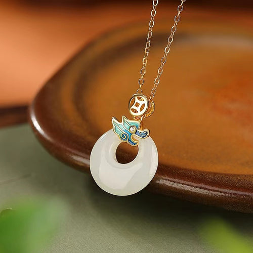Gold-plated dragon and blue enamel white jade pendant resting on the edge of a wooden tray.