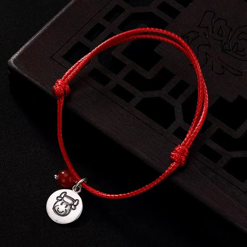 Adjustable red string bracelet with a silver Ox zodiac charm and polished red bead.