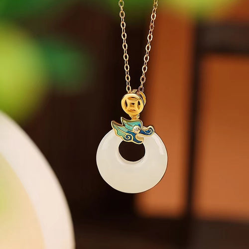 White jade ring pendant with gold-tone dragon, coin, and blue enamel cloud details on a warm backdrop.