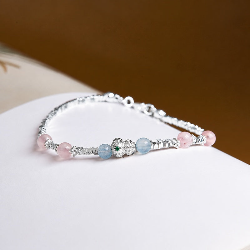 Aquamarine and rose quartz gourd bracelet resting on a book, oblique view
