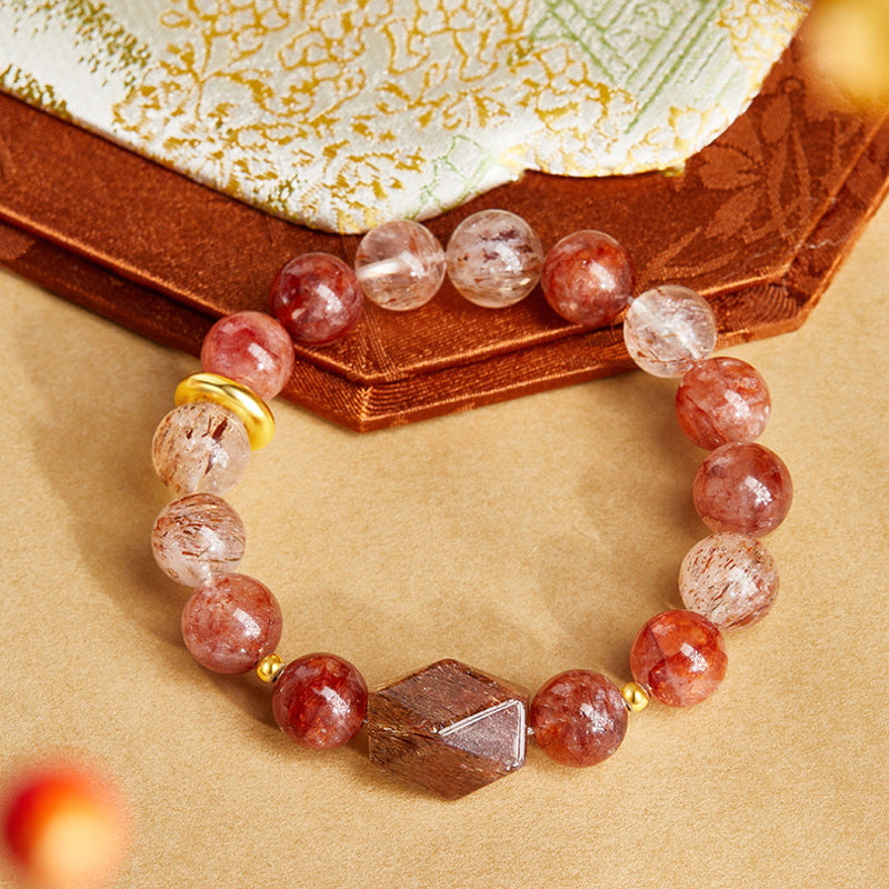 Overhead view of red inclusion quartz bracelet resting beside embroidered fabric