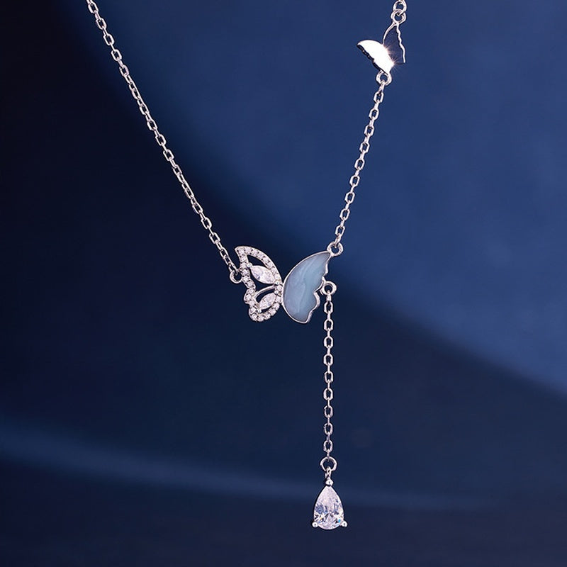 Blue enamel butterfly silver necklace with a clear teardrop against navy fabric