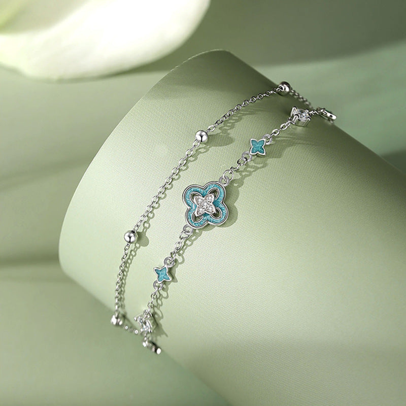 Blue enamel clover bracelet resting on a green ribbon