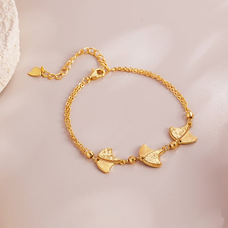 Gold-colored sterling silver ginkgo leaf bracelet on a soft blush background