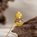 Gold-colored heart gourd necklace resting upright on natural wood