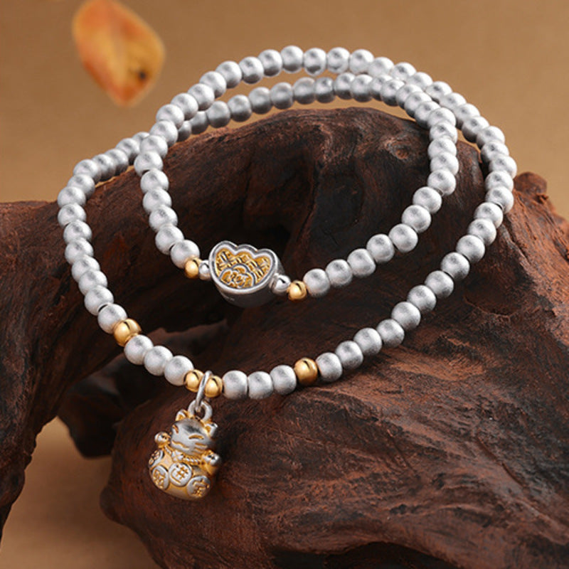 Lucky cat silver bracelet arranged across dark natural driftwood