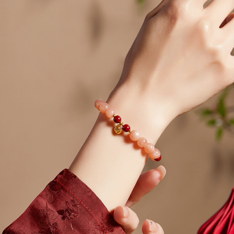 Supplier model wearing peach moonstone bracelet with a gold colored fortune bag