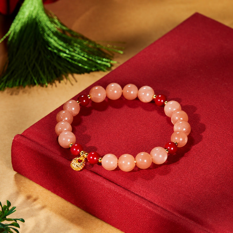 Peach moonstone bracelet with fortune bag charm arranged on red fabric