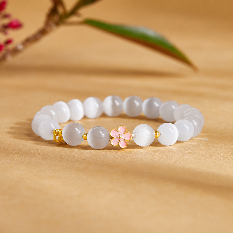 Peach blossom cat-eye glass bracelet resting on a warm ochre background