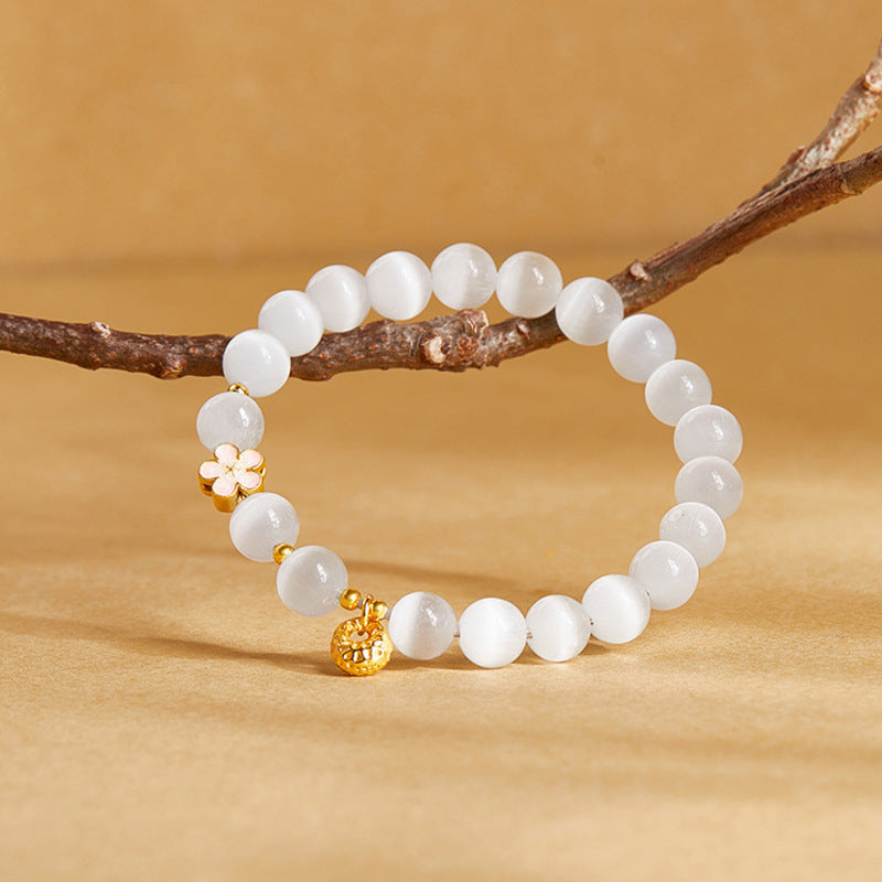 Bracelet resting against a branch showing pink flower and blessing pouch