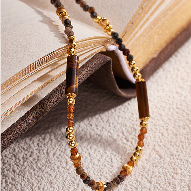 Pietersite and Orange Garnet necklace draped over a warm-toned book