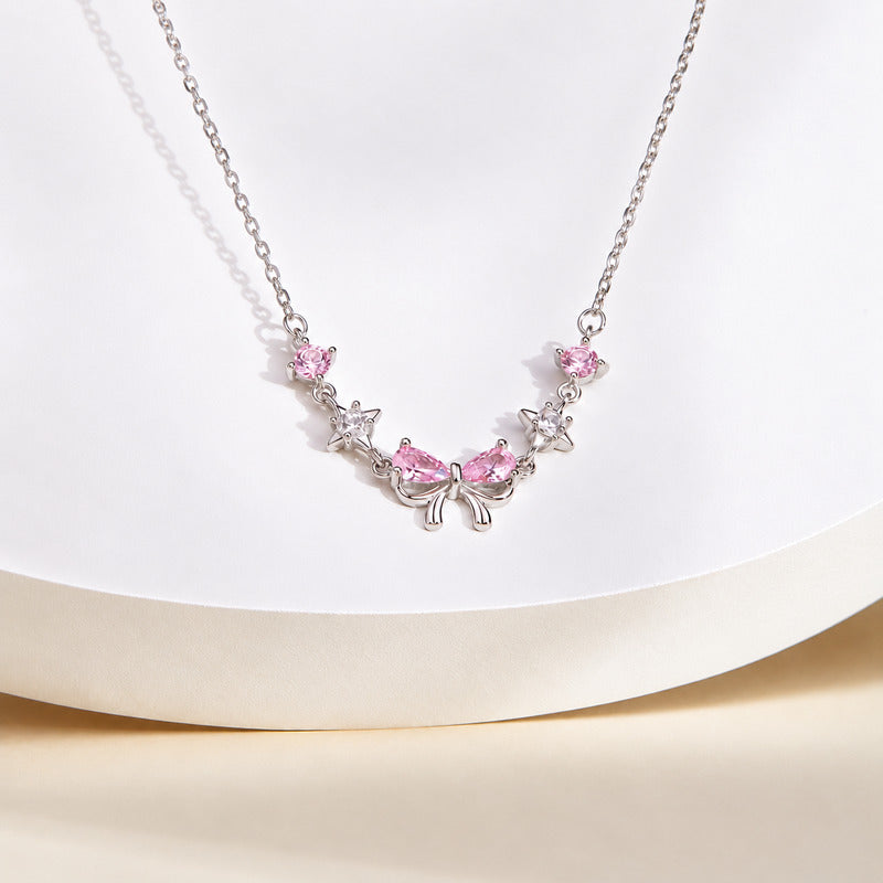 Pink bow sterling silver necklace on a curved white display with warm cream background