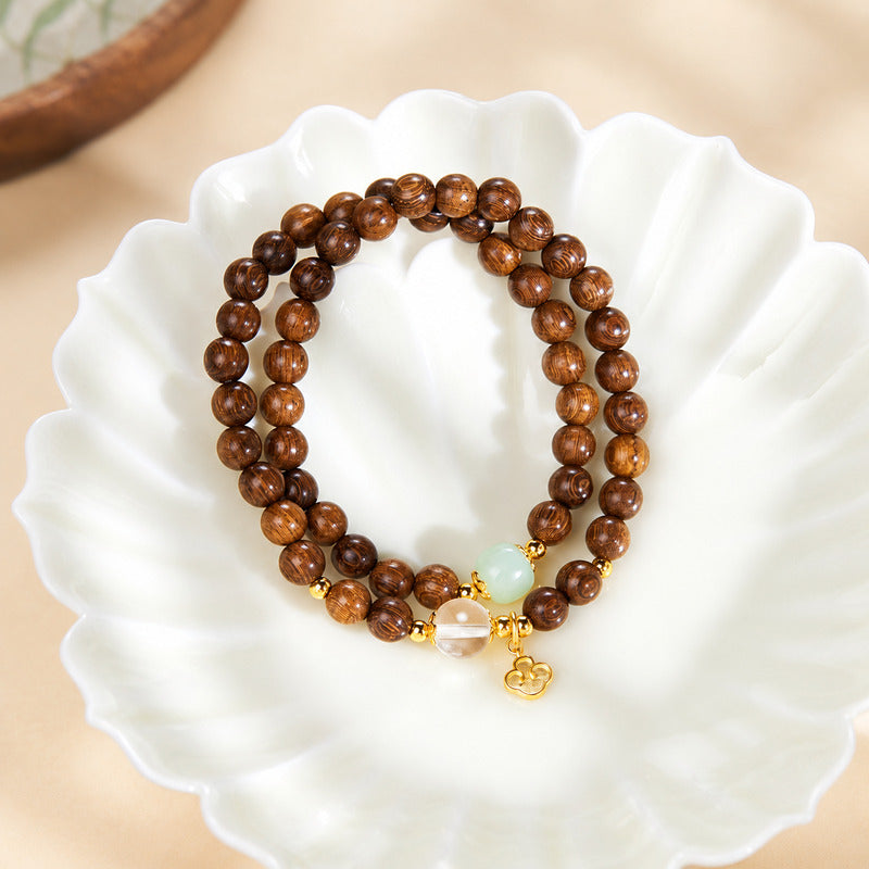 Ruyi Golden Silk Sandalwood double-wrap bracelet on a white leaf-shaped dish