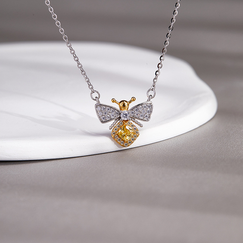 Silver bee pendant necklace with yellow cubic zirconia on a white tray