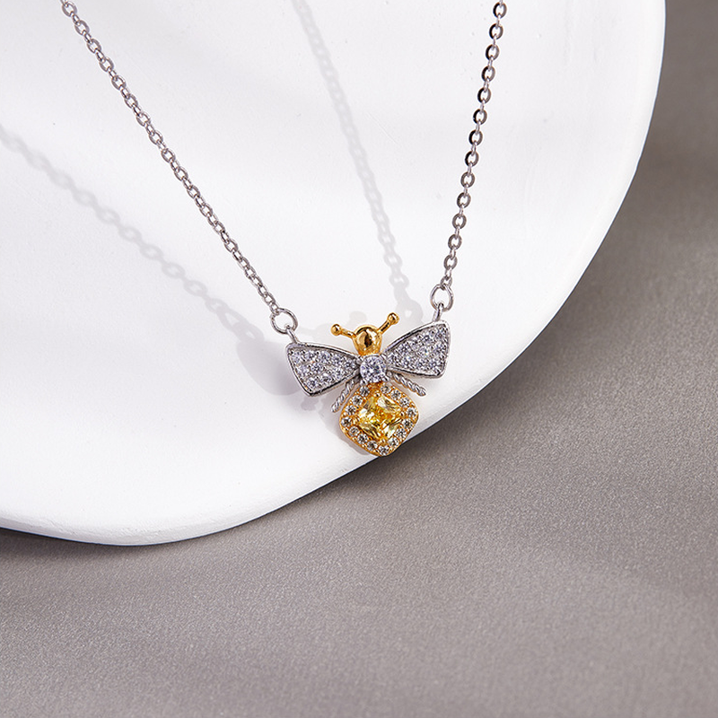 Silver bee necklace with clear wings on a white tray, angled view