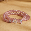 Pink strawberry crystal double wrap heart bracelet resting on a warm golden background