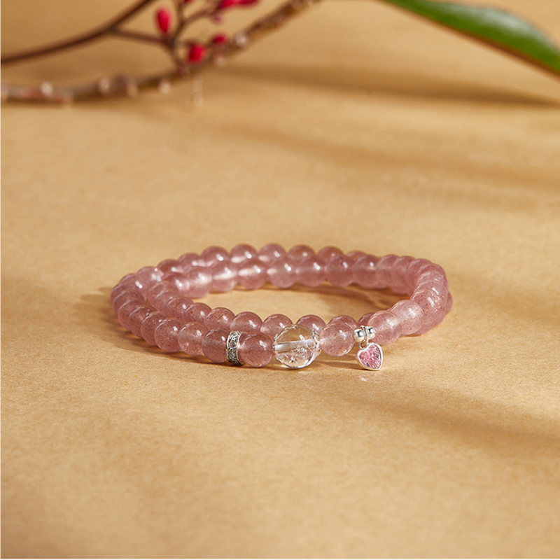 Strawberry crystal heart bracelet with clear quartz bead resting beneath a flowering branch