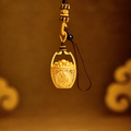 Gold-plated brass wealth basket charm with ingot details suspended against a warm golden background