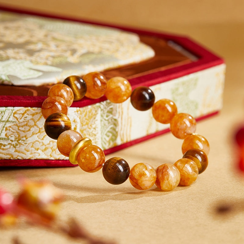 Golden quartz bracelet leaning against a patterned box with tiger's eye beads