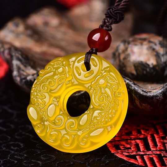 Close-up of translucent yellow jade Pixiu pendant showing carved scrollwork around circular opening