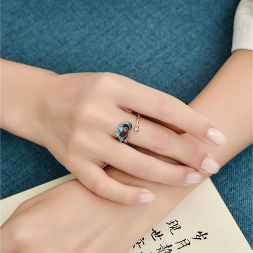 Person wearing a blue cloisonne lotus silver ring while resting hands on a book