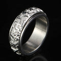 Silver-tone titanium spinner ring with raised six-word mantra symbols against a glossy black background