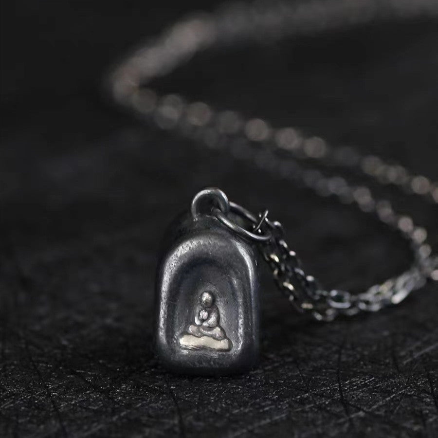 Vintage 925 silver arched Buddha pendant necklace resting on dark textured surface